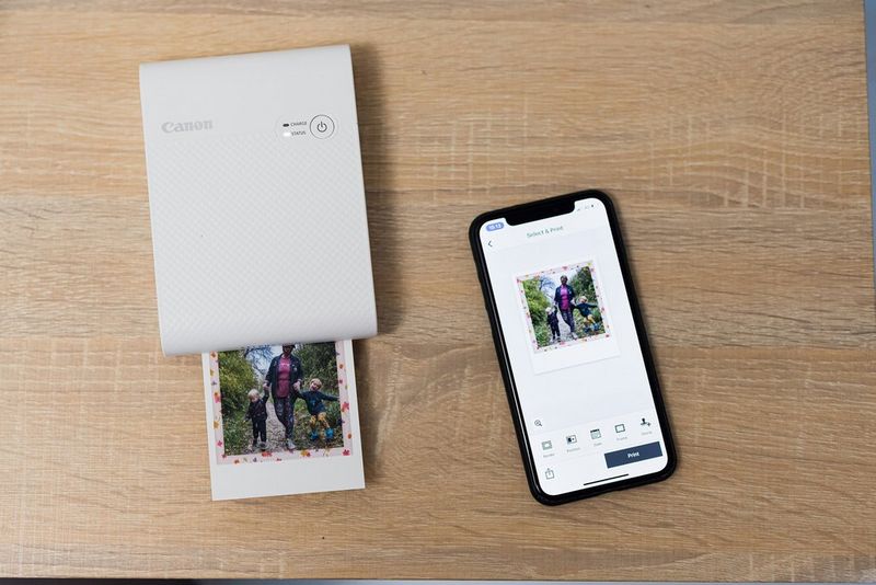 A Canon SELPHY Square QX10 next to a smartphone.