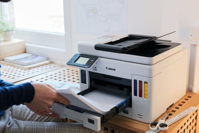 A user adds paper to the cassette at the front of a Canon MAXIFY printer.