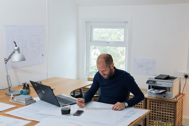 A man works at a desk in an architect's office with a Canon MAXIFY printer on a cupboard in the background.