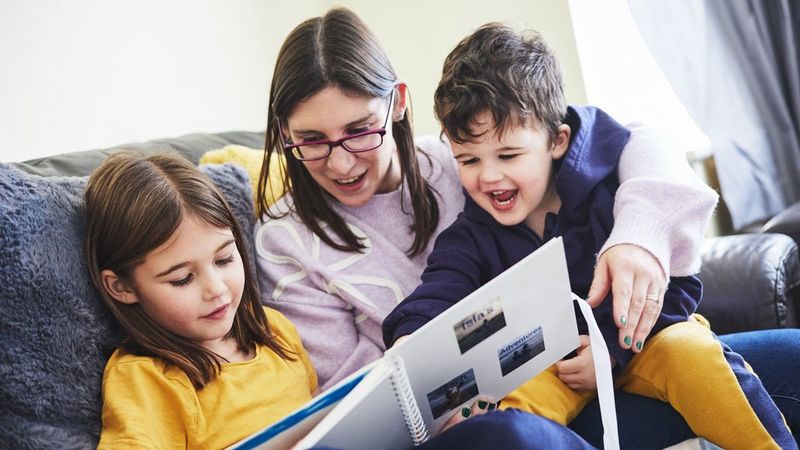 An adult and two children sit on a couch, looking through a handmade storybook created using a Canon SELPHY CP1500 and the Canon SELPHY Photo Layout app.