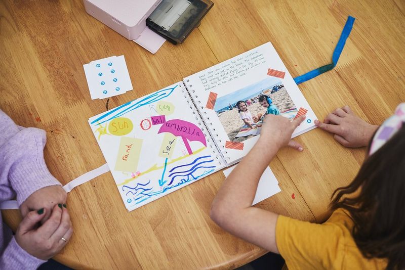 A child puts washi tape across the corner of a photo in a scrapbook, created using a Canon SELPHY CP1500 printer and the Canon SELPHY Photo Layout app.