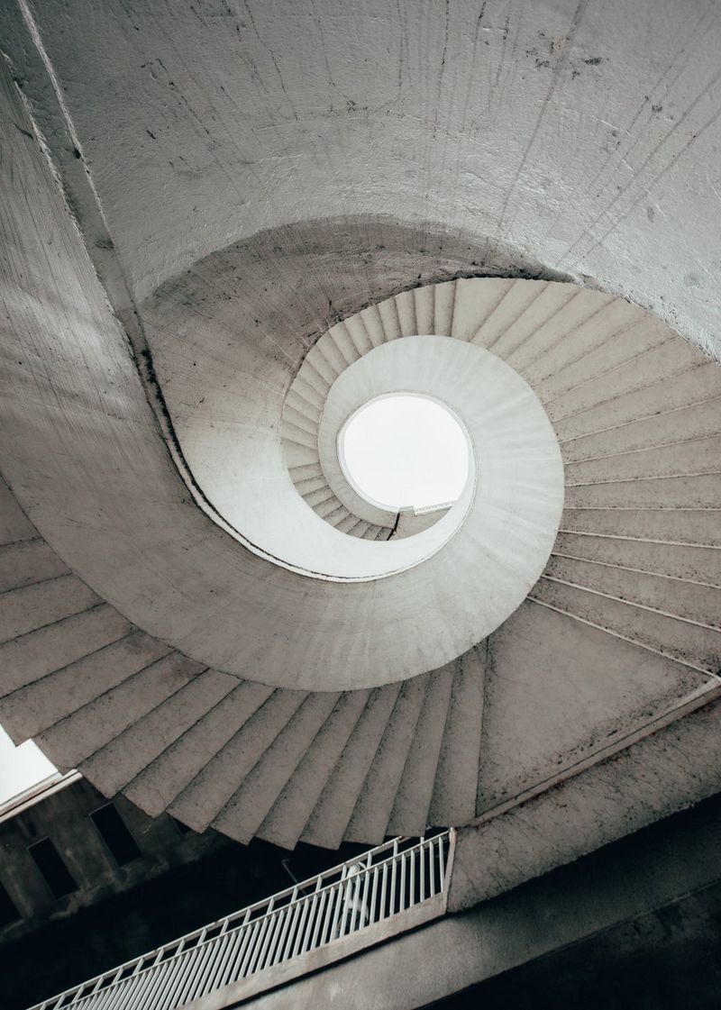 An image shot upwards of a concrete spiral staircase, which forms a winding, shell-like pattern.