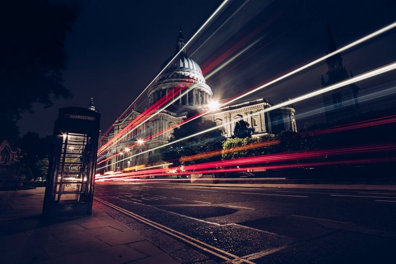 A London street at night, with a red telephone box in the foreground and St Paul's Cathedral in the background, and long light trails of red, white and yellow running along the road between them.