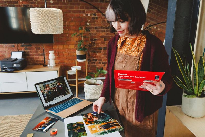 Een selectie van geprinte trouwfoto's voor een open laptop, terwijl een vrouw achter de laptop een foto bestudeert die net is geprint.