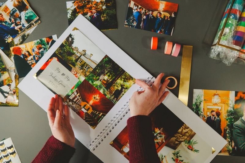 A pair of hands arranges a page with four scene-setting images, opposite a page with two larger photos of the wedding set-up.
