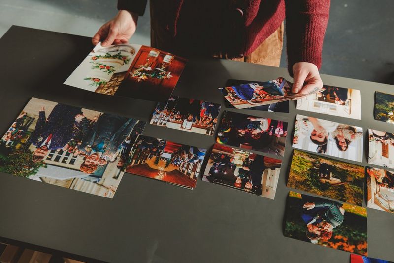 A person lays out wedding prints of different sizes on a table, holding two up to examine them closer.