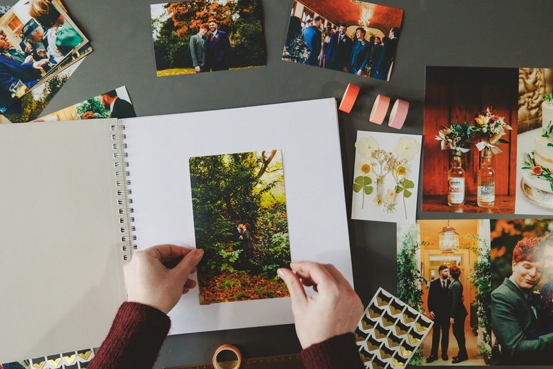 A pair of hands arrange an image of two grooms embracing on the first page of a homemade wedding album.
