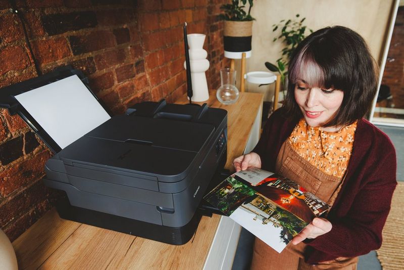 A woman stands in front of a Canon PIXMA printer, examining photos that have just been printed.