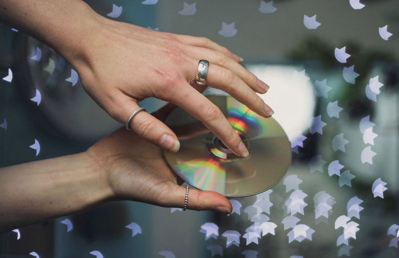 A person placing their hand onto the shiny side of a CD, with bokeh star shapes surrounding them.
