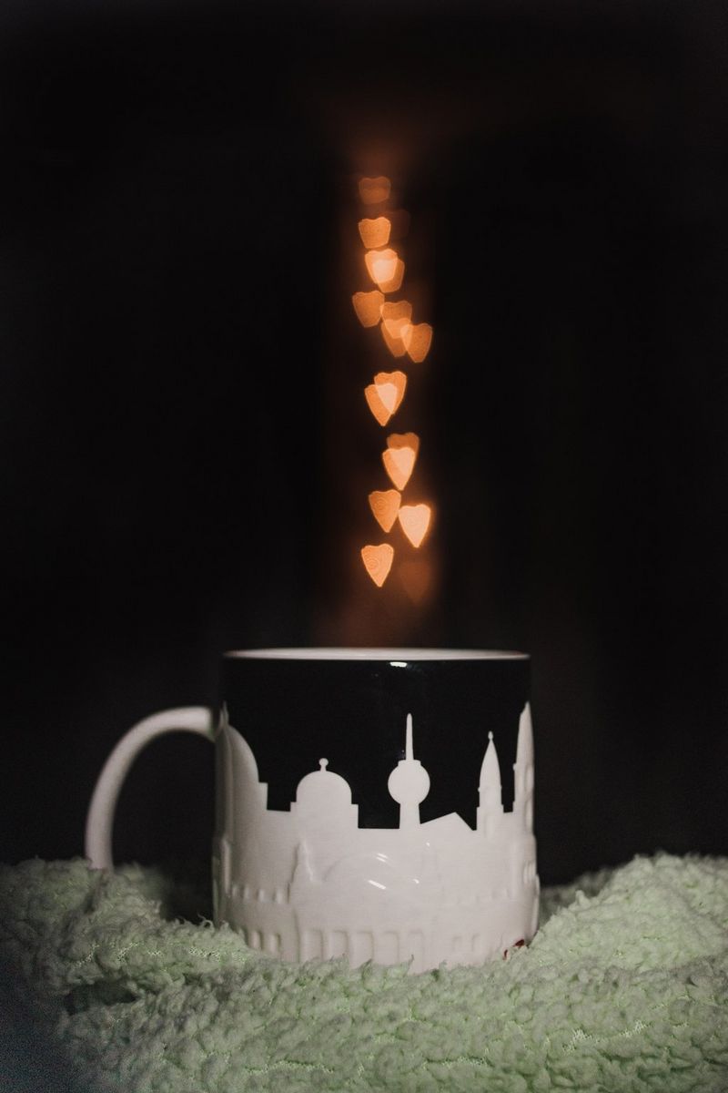 A trail of bokeh love hearts appear to be floating in the steam above a black and white mug.