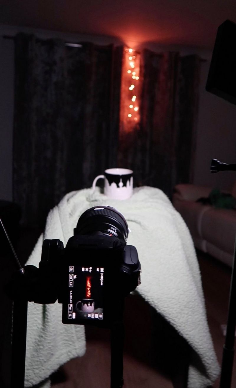 A camera on a tripod positioned in front of a mug and a string of fairy lights.