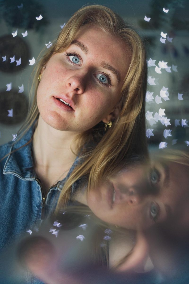 A self-portrait of a woman with star-shaped bokeh made from fairy lights clustered behind her, with a reflection of her face visible in the foreground.