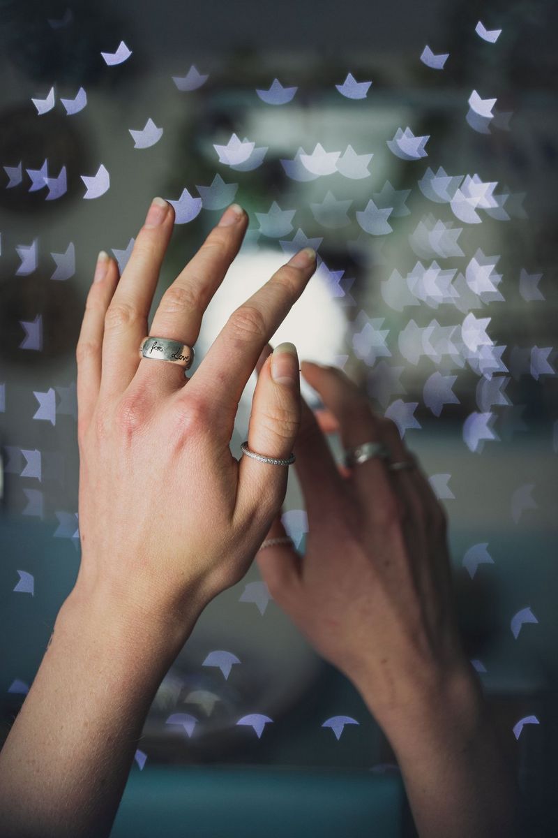 A pair of hands wearing rings, with star-shaped bokeh in the background.