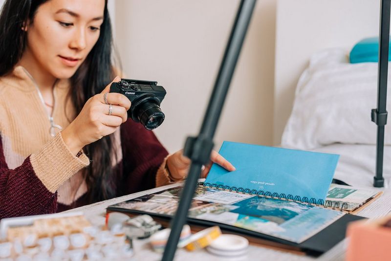 Uma mulher a tirar uma fotografia de um álbum de recortes de cima com uma câmara Canon PowerShot G7 X Mark III.