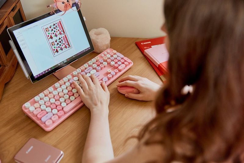 A woman typing on a pink and white computer keyboard.