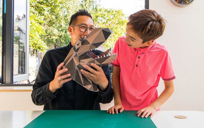 An adult and a child admire a model T-rex head built from a Canon Creative Park template, which is held by the adult.