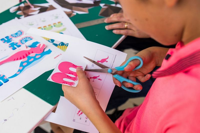 A child uses a pair of scissors to cut out a dinosaur template downloaded from Canon Creative Park and printed using a Canon PIXMA printer.