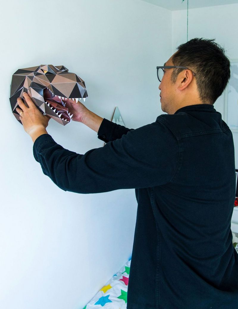 An adult attaches a papercraft T-rex night light to a white bedroom wall.