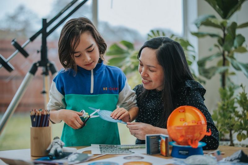 A mother helps her son use a pair of scissors to cut a space-themed papercraft template from Canon Creative Park.