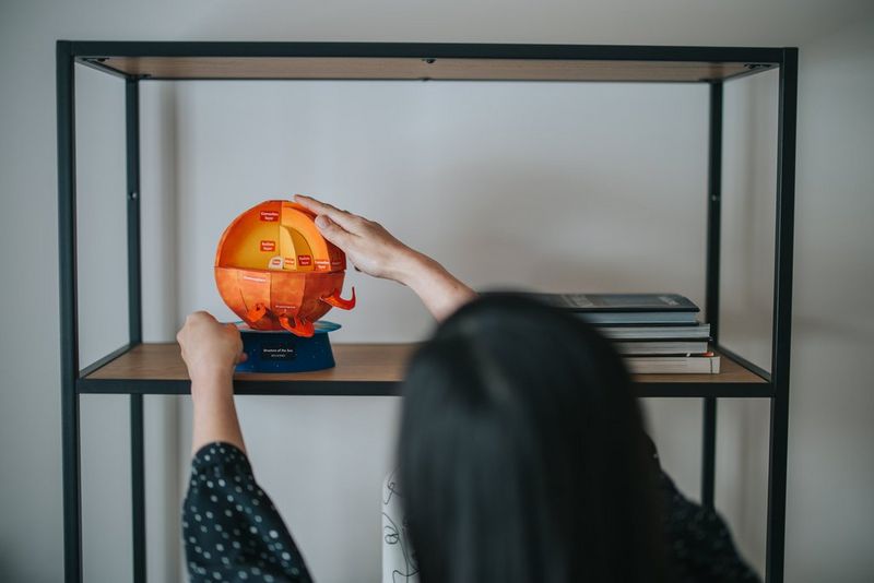 A person places a papercraft Sun, created from a Creative Park template, on a shelf.
