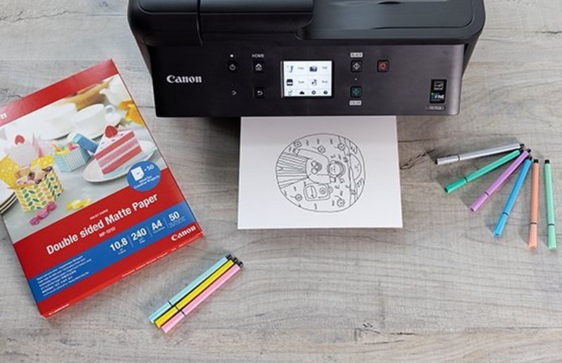 Black Canon PIXMA printer with a colouring printout and print paper on a desk.