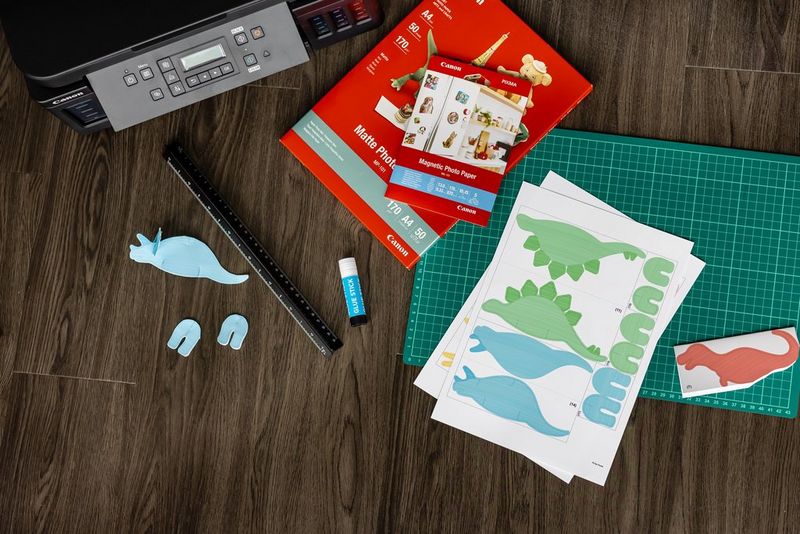 A PIXMA G6050 printer and Magnetic Photo Paper next to a cutting board, and templates for a papercraft dinosaur mobile.