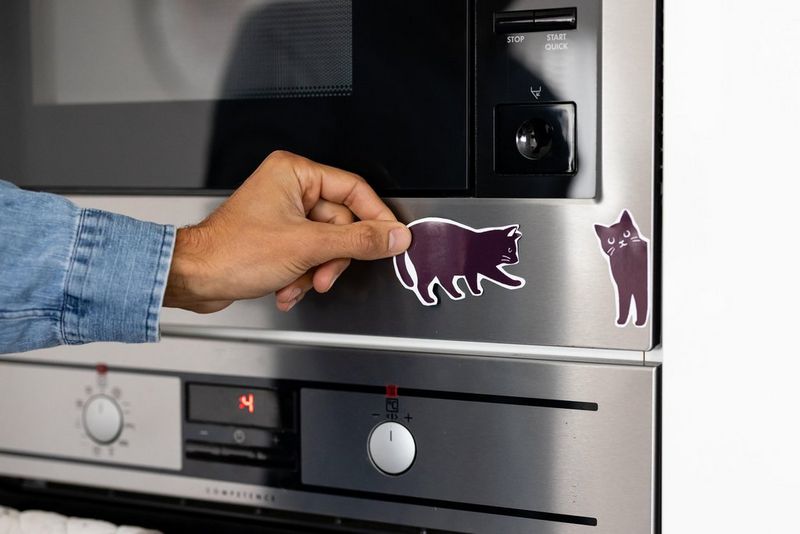 A hand placing black cat magnets on a cooker front.