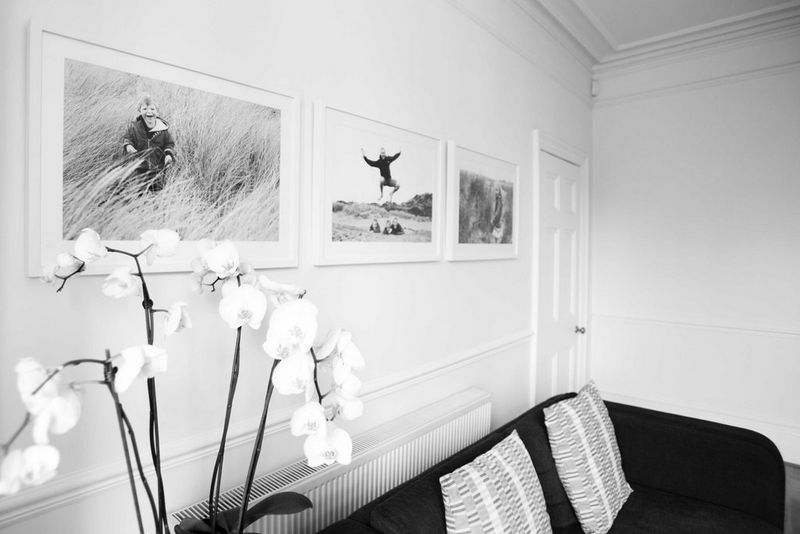 A black and white image of three framed prints displayed on a wall above a sofa, with a white orchid on the table in front.