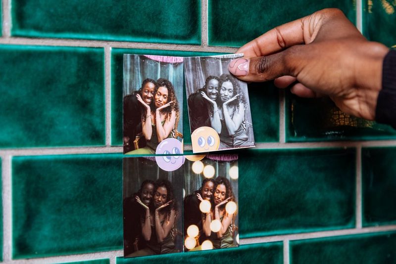 A person's hand sticks images of two women on to a green tiled wall. The photos were printed using a Canon Zoemini S2 and the Canon Mini Print app. 