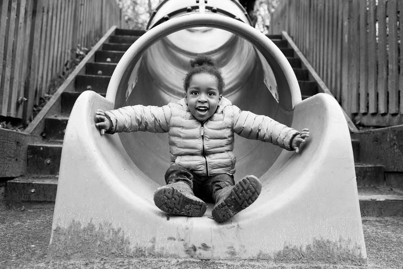 A little girl smiles, with her arms outstretched, at the bottom of a slide.