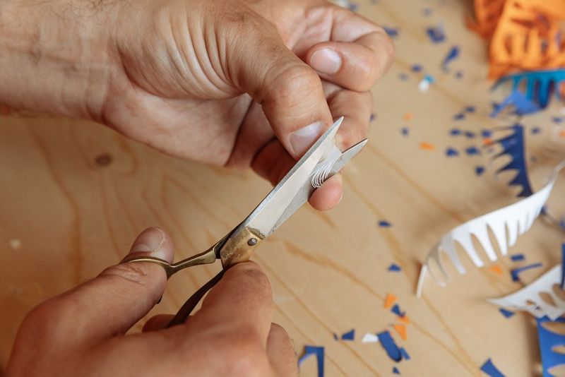 A pair of hands uses a pair of scissors to cut a paper feather.