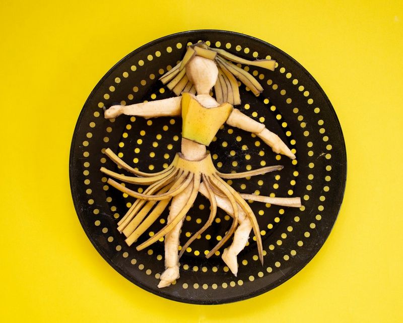 A banana cut and moulded into the shape of a woman in a hula skirt positioned on a black plate with yellow spots. 