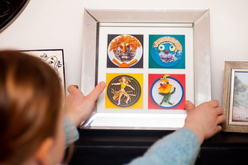 A young girl placing a collage of food face images set in a frame on a mantelpiece.