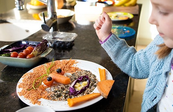 A young girl creating a face out of food on a plate. 