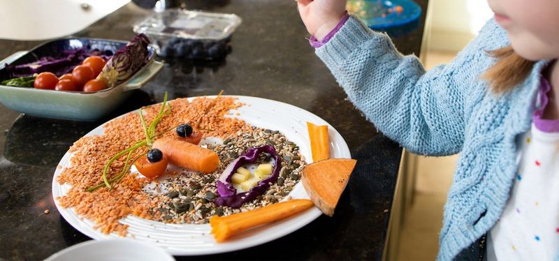 A young girl creating a face out of food on a plate. 