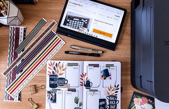 A top-down image of a selection of colourful exercise books, a calendar, stickers and Canon printer paper.