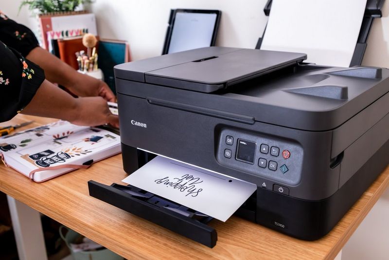 A Canon PIXMA printer sits on a desk, printing out a shopping list.