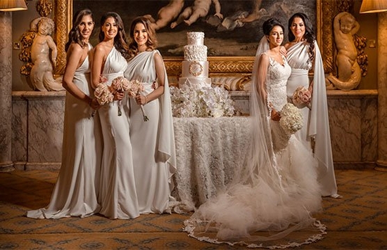 A group portrait of a bride and her bridesmaids posing next to a tiered wedding cake.