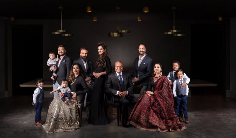 A large family group dressed in formal wear, posed in a dimly lit room with golden ceiling fixtures.