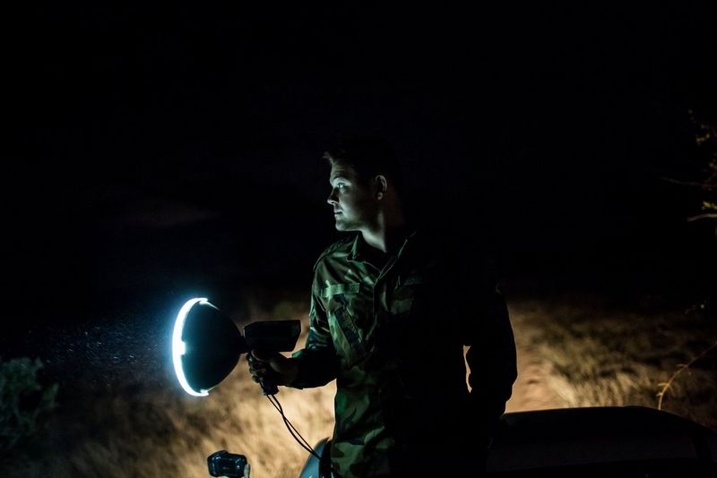 A South African anti-poaching ranger uses a large torch to look for movement in an outdoor enclosure at night.