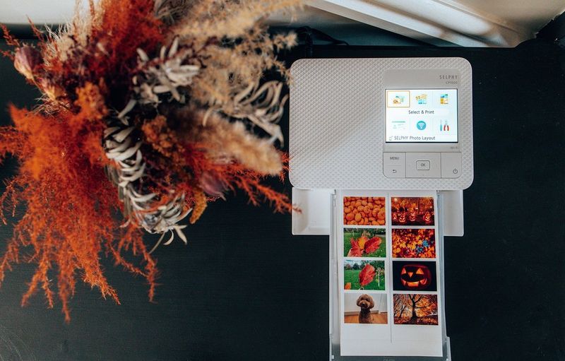 A sheet of autumn-themed images emerging from a Canon compact printer.