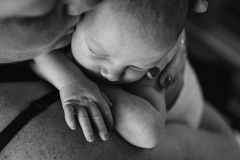 A black and white close-up shot of a mother kissing a sleeping baby she is holding to her shoulder.