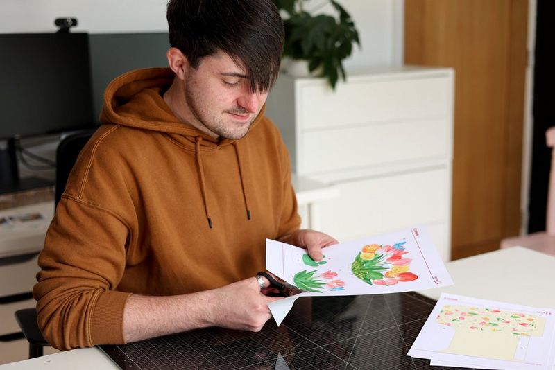 A young man sits at a table cutting out a card template printed from Canon Creative Park.