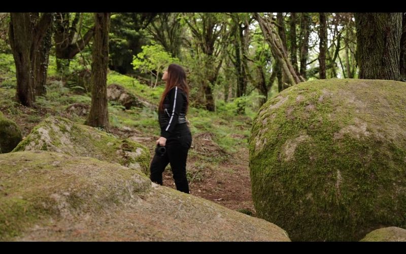 A woman walking between mossy rocks in a forest. 