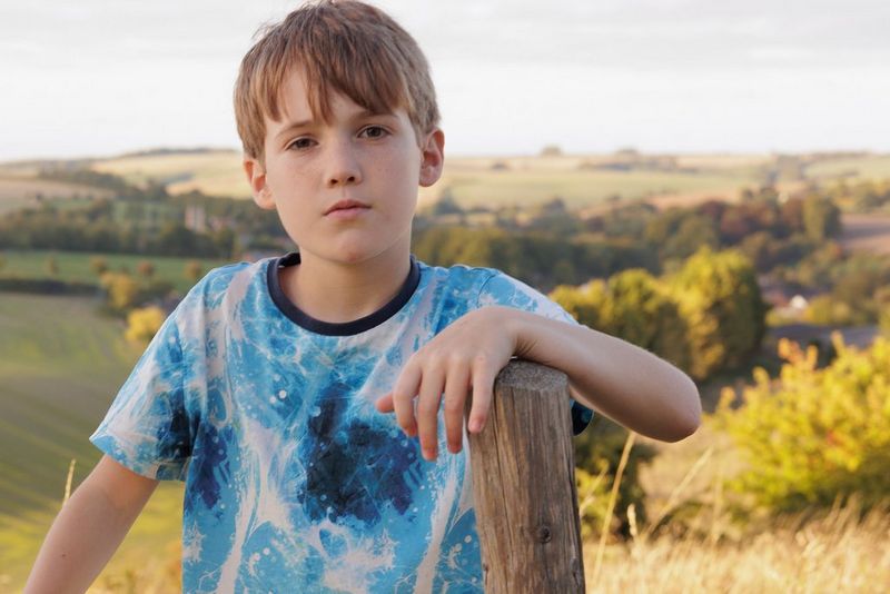 A child in a field resting his arm on a wooden post. A reflector has been used to shade his face. Taken on a Canon EOS R6 with a Canon RF 50mm F1.8 STM lens. 