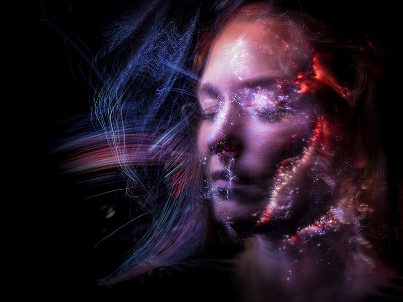 A close-up shot of a woman's face covered in multi-coloured trails of light, shot on a Canon EOS R6.