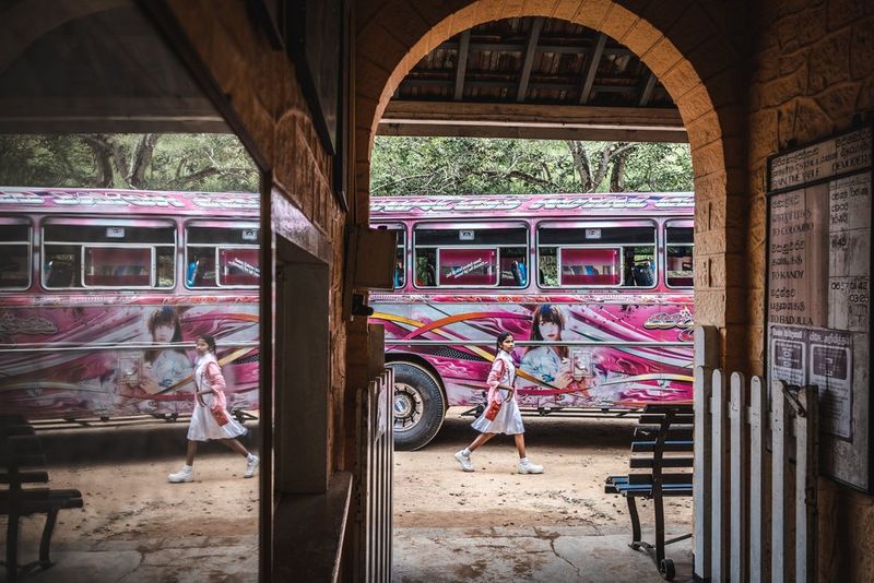 Taken through a mirrored archway, a young girl walks past a single-decker bus painted in vivid pink, yellow, white and red, with the scene reflected on the left of the frame. Taken by photographer Martin Bissig on a Canon EOS R10.