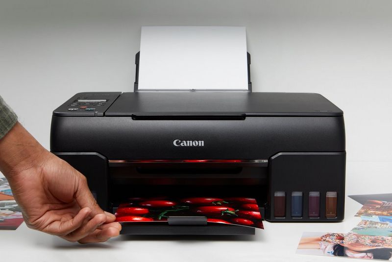 A hand picking up a photo of some tomatoes that has just printed out of a PIXMA G series printer.
