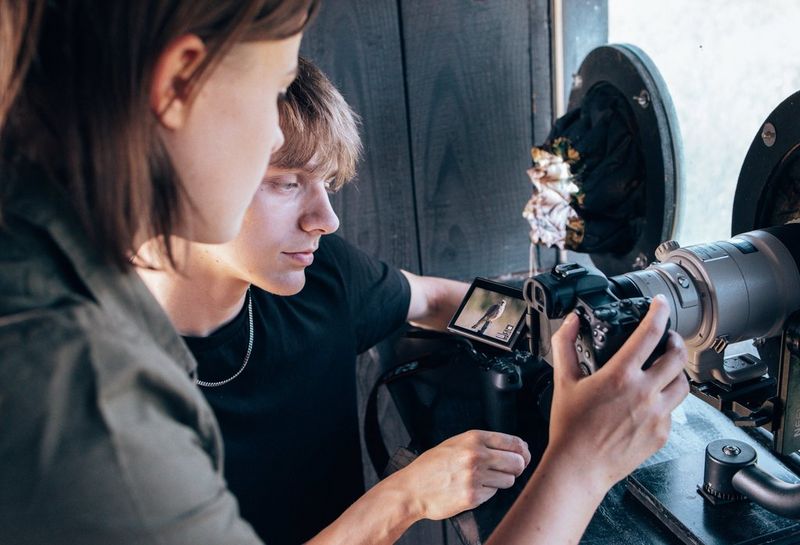 In a bird hide, two young people study a picture of a kestrel sitting on a wooden post on a camera touchscreen.