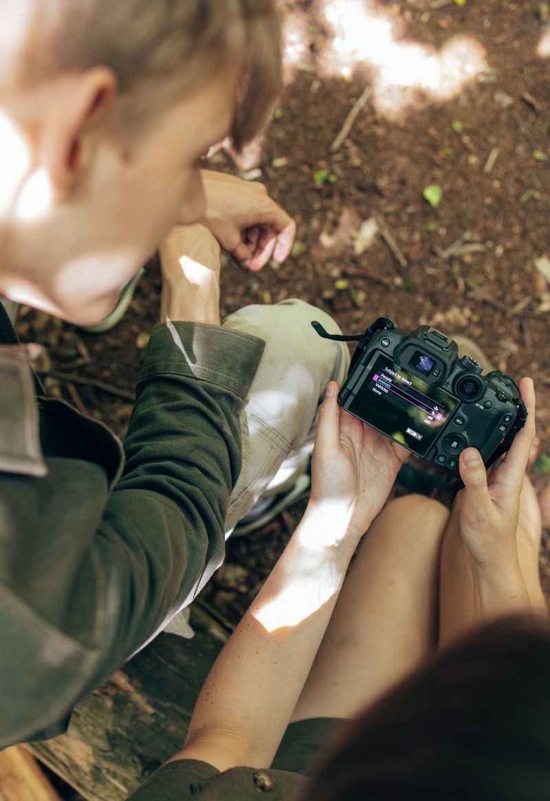 Two seated young people adjust the settings on a Canon camera, in this image shot from above.